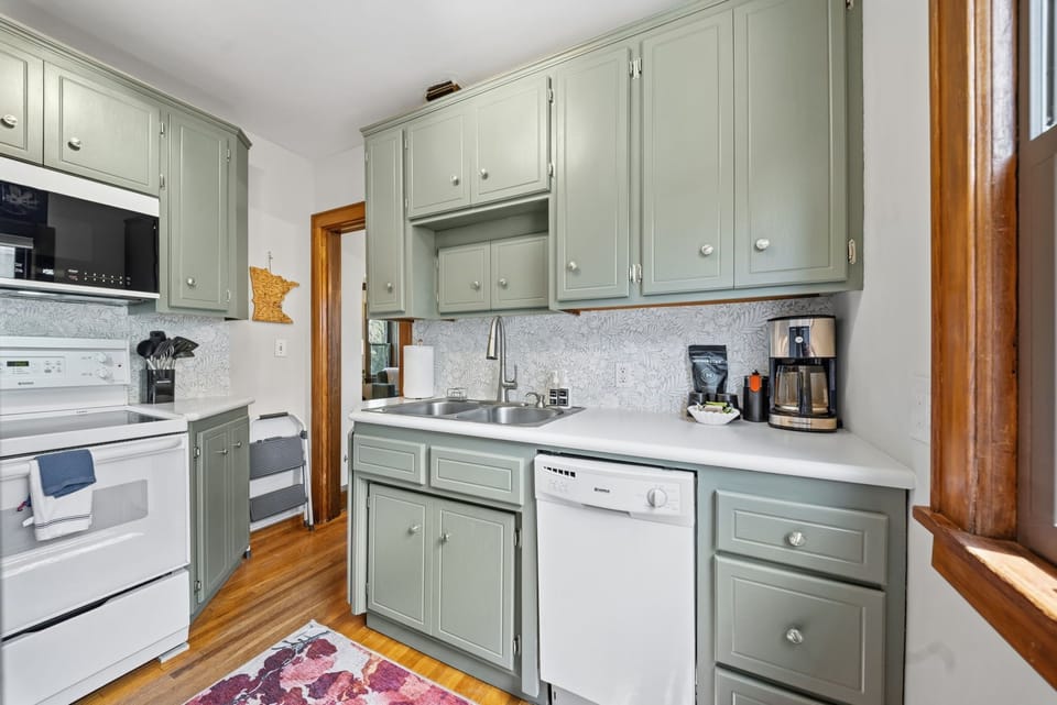 Your fully equipped kitchen with sage-green cabinetry and warm wood floors invites easy meal prep after exploring the area.