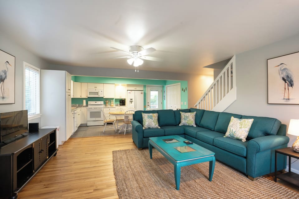 Unwind in your inviting open-concept living area, where coastal colors and comfortable seating blend seamlessly with a fully-equipped kitchen, perfect for gathering after beach adventures.