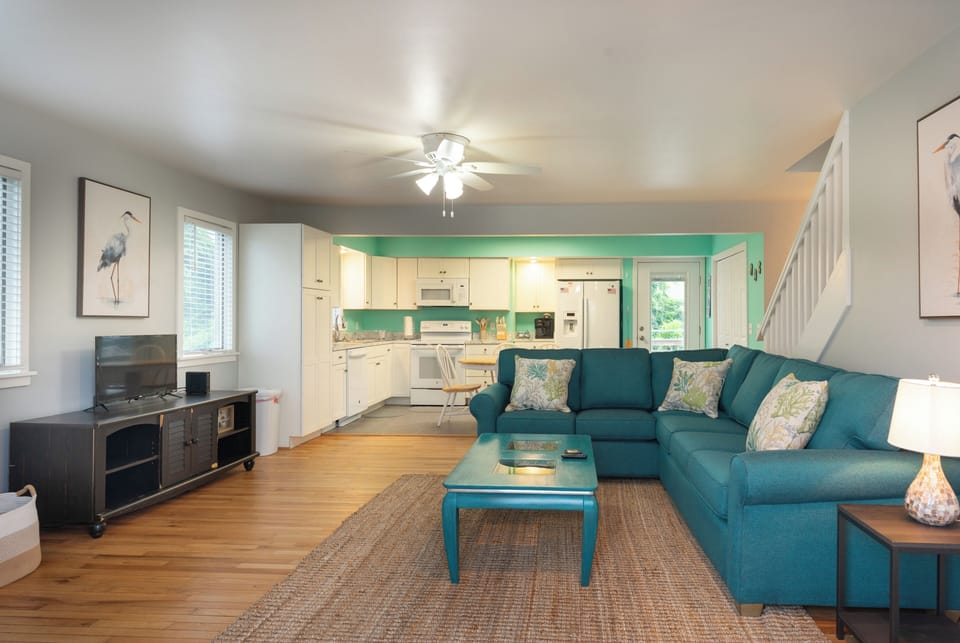 Sink into the plush teal sofa and unwind in your open-concept retreat, where coastal-inspired pops of color meet warm wood floors and a fully equipped kitchen ready for your morning coffee.