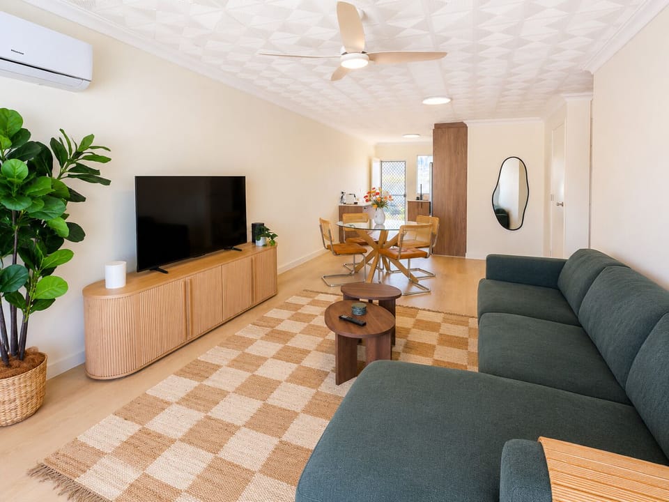 Bright open-plan lounge with large TV, dining nook, and stylish decor
