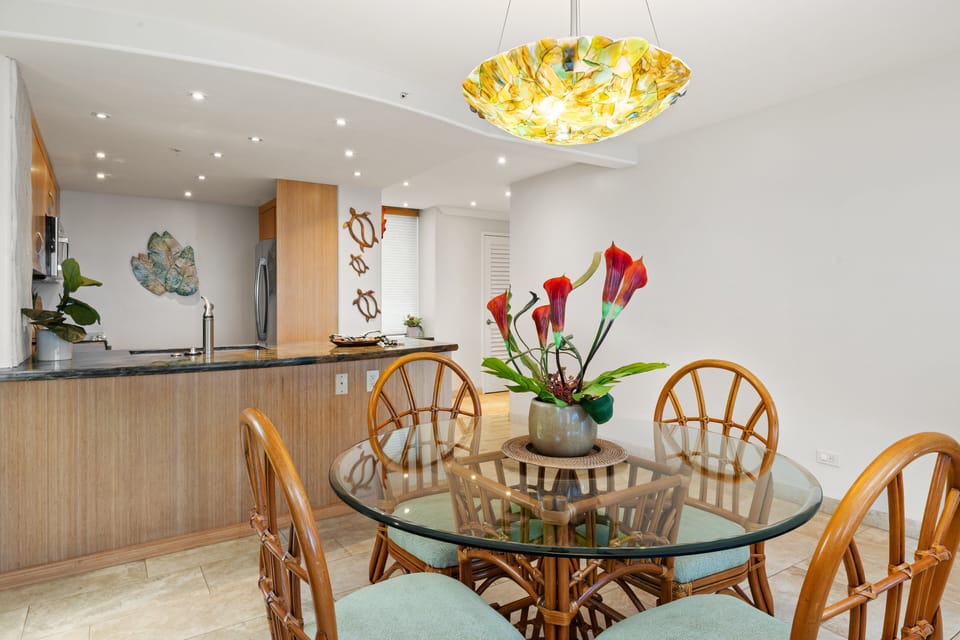 Enjoy casual meals or lively conversation at the glass-top dining table, elegantly lit by a colorful custom pendant light.