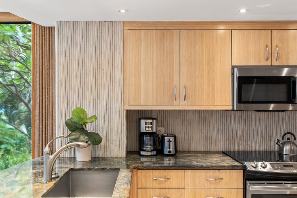 A close-up view of the kitchen featuring light wood cabinetry, sleek granite countertops, stainless steel appliances, and a deep undermount sink.