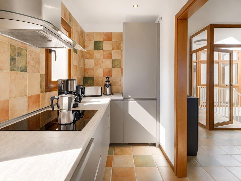 Sleek and modern galley kitchen featuring grey flat-panel cabinetry, a glass cooktop, rustic terracotta wall tiles, and premium stainless steel coffee appliances.