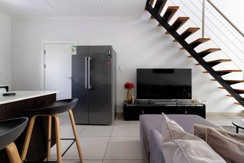 Modern loft-style lounge with smart TV, bar seating, and sleek fridge
