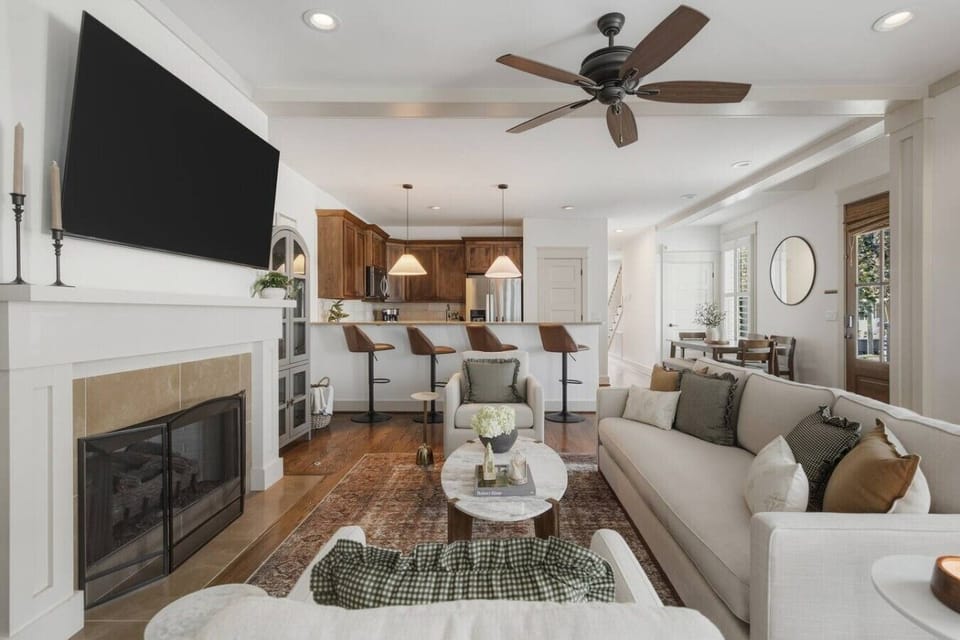 Beautifully designed living room with a fireplace, ceiling fan and plenty of comfy seating. Smart TV, wood floors, and easy flow into the kitchen.