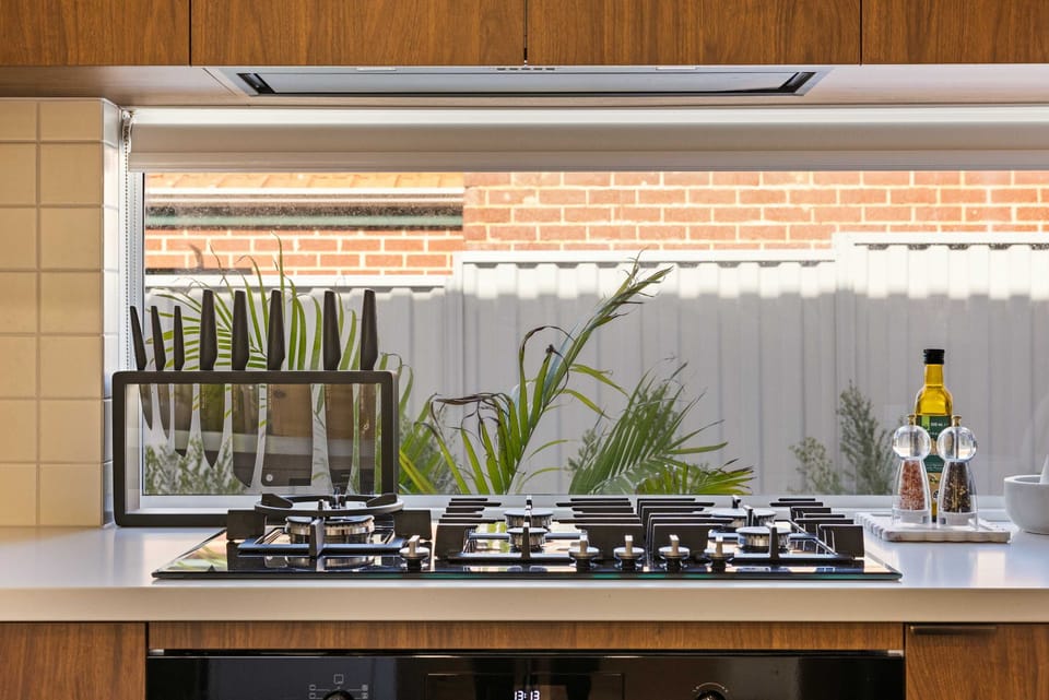 Prepare delicious meals with ease using this modern gas cooktop, set against a stylish window backsplash offering natural light and garden views. 