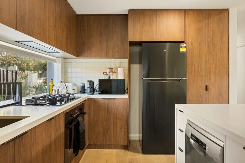Cook up culinary delights in this fully equipped kitchen featuring sleek wood-finish cabinetry, modern stainless steel appliances, a gas stovetop, and clean white countertops. 