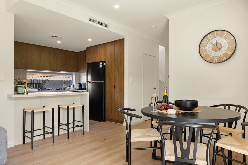 Dine together in this modern open-plan dining and kitchen area, complete with a round table, breakfast bar seating, and warm wood cabinetry. 