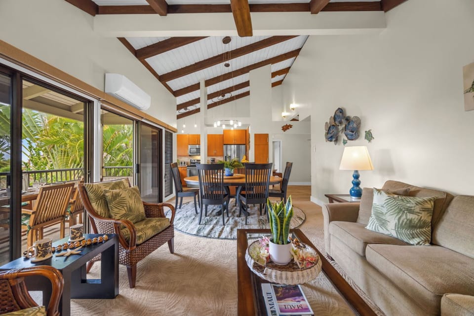 Unit 1:Step into a spacious living and dining area featuring vaulted ceilings with exposed beams, cozy seating, and large sliding doors that open to the lanai.