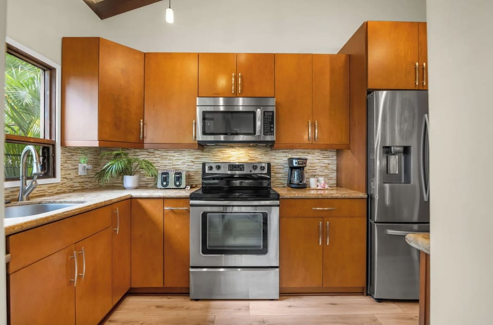 Unit 1:Cook with ease in a modern kitchen equipped with stainless steel appliances, warm wood cabinetry, and a stylish tile backsplash.