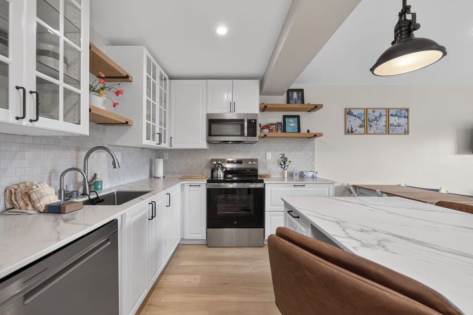 Your home away from home features a bright, fully equipped kitchen with modern appliances, marble countertops, and open shelving—perfect for preparing meals together or enjoying morning coffee in comfort.
