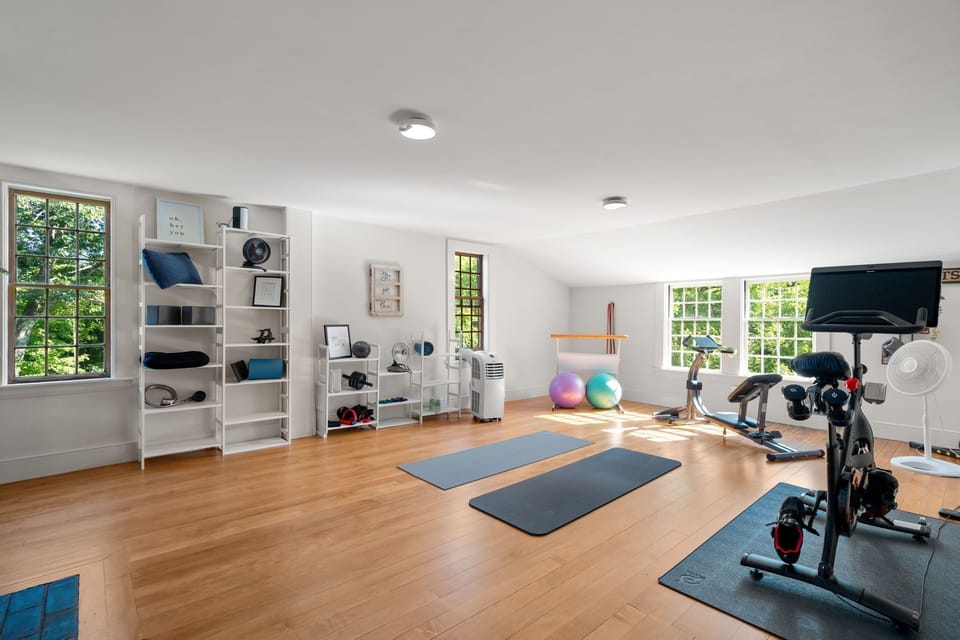 A bright home gym with exercise equipment, yoga mats, and light wood flooring.