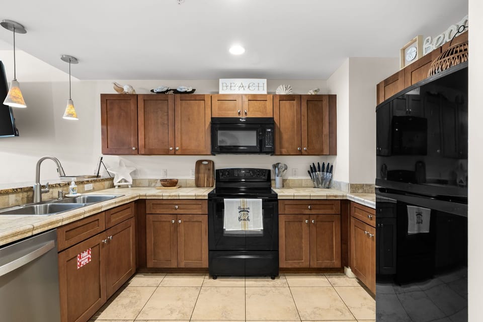Your fully equipped kitchen invites you to cook up a feast with granite counters, stainless sink, and modern black appliances—all set in a warm coastal vibe.