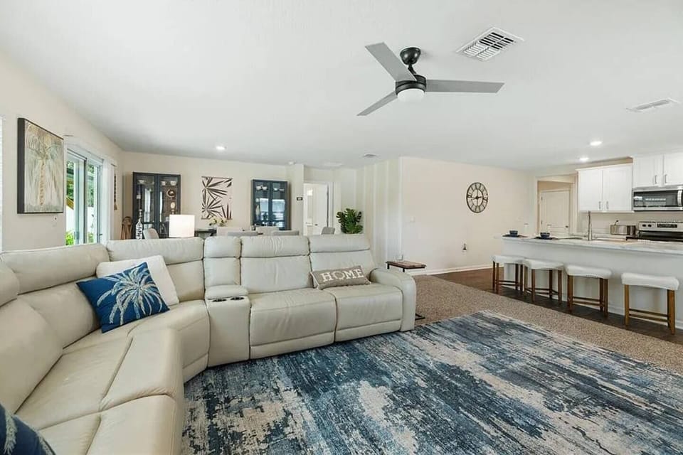 Spacious open-concept living room with coastal décor, plush sectional sofa, and ceiling fan — flows directly into the kitchen for easy entertaining.