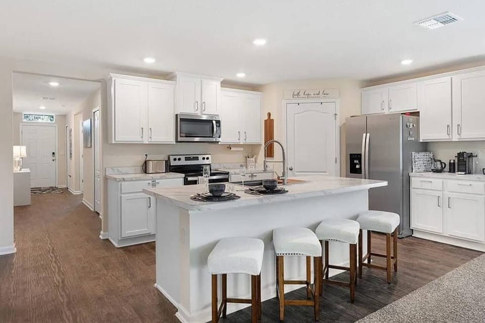 Fully equipped chef's kitchen with quartz island, bar seating, stainless steel appliances, coffee station, and ample cabinet storage.
