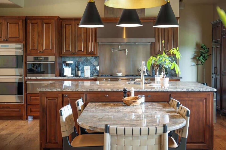 The chef’s kitchen stuns with vaulted wood-beam ceilings, a gas cooktop, double ovens, and luxe granite counters. A central island with seating, high-end appliances, and designer lighting make this space perfect for cooking, gathering & entertaining