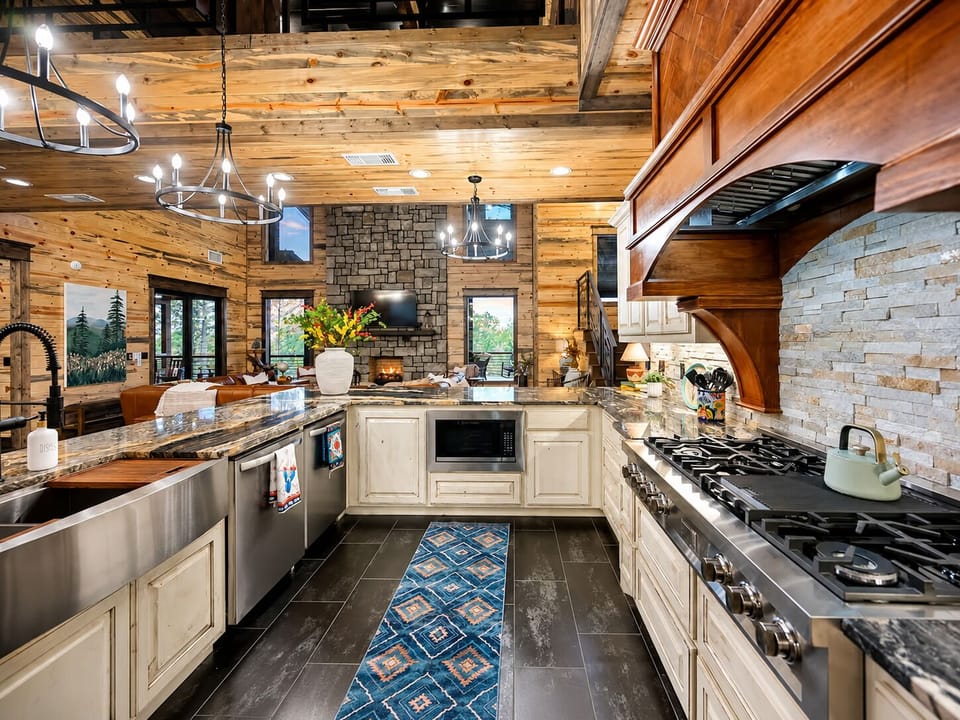 Spacious kitchen with a gas range, dual sinks, dual dishwashers, microwave, custom cabinetry, stone backsplash, and open views toward the living room.