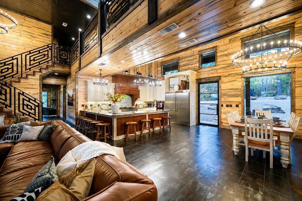 Spacious open-concept kitchen, dining, and living area with a large island, bar seating, dining table, high ceilings, and warm wood finishes.