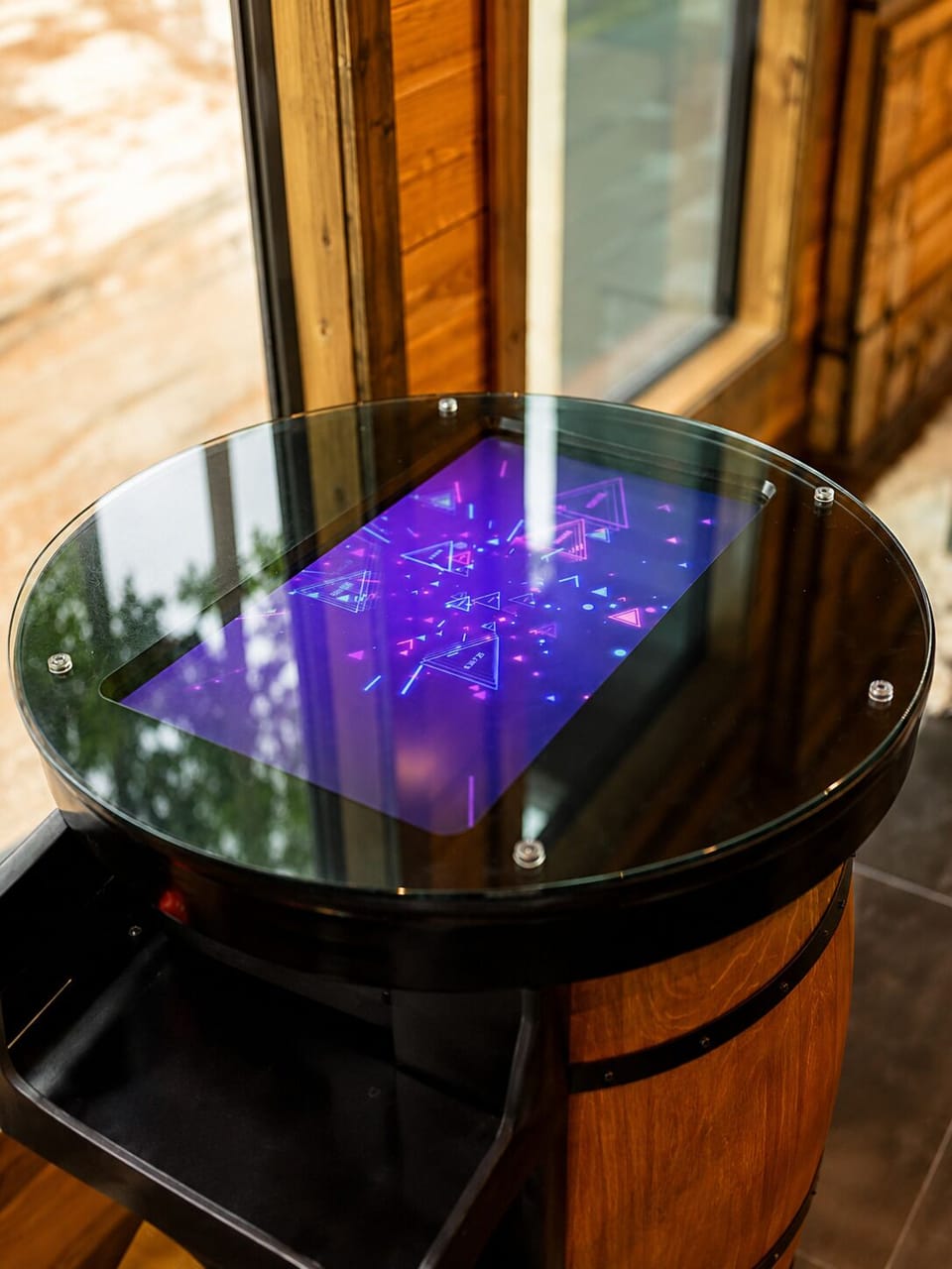 Barrel-style game table with an interactive digital screen and glass tabletop.