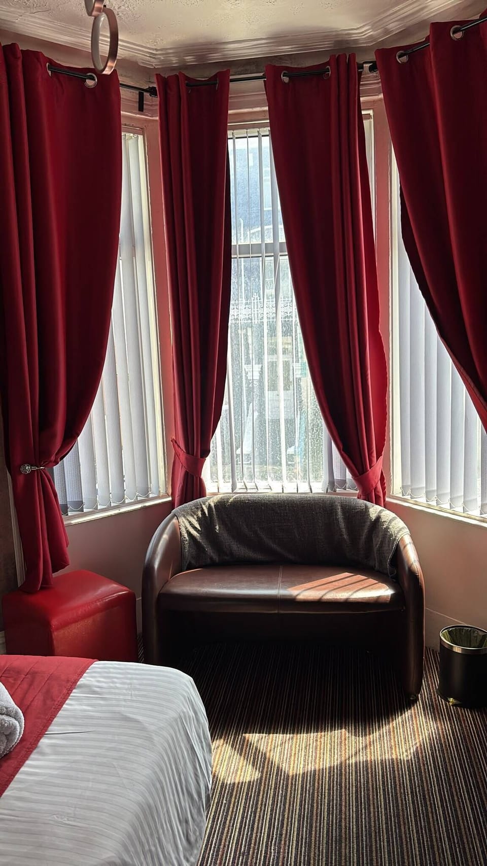 Sunny bay window nook with loveseat and rich red curtains