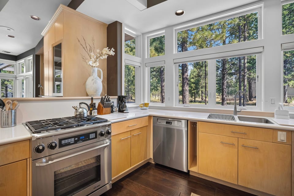 Cook surrounded by towering pines and dappled sunlight streaming through expansive windows. This bright kitchen invites you to prepare meals while feeling completely immersed in nature's peaceful embrace.