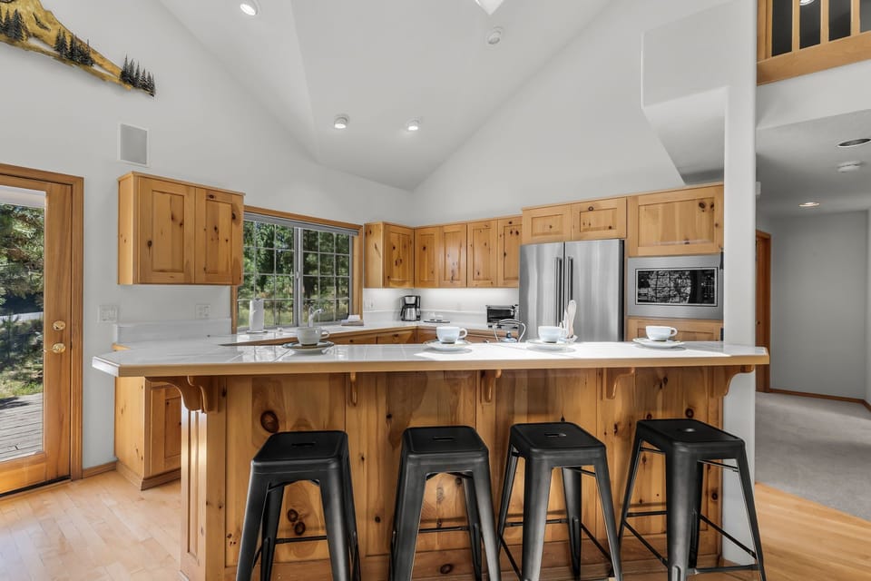 This kitchen invites you to gather around the spacious island with rustic pine cabinetry and modern stainless appliances, perfect for preparing meals with mountain views streaming through the windows.