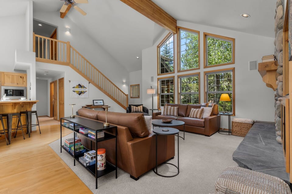 Step into this open, sun-drenched living space where soaring ceilings and oversized windows frame stunning forest views. Sink into cozy leather seating, enjoy the warmth of stone accents, and feel the inviting flow between kitchen and lounge.