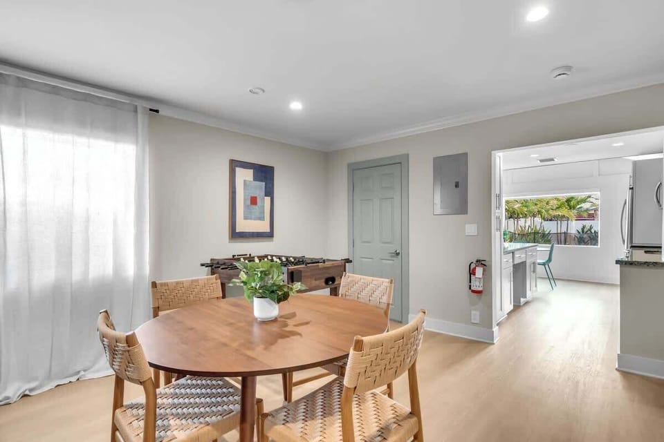 Dining area with a round table for four, woven chairs, and a foosball table nearby. Bright and open, flowing into the kitchen for easy entertaining.