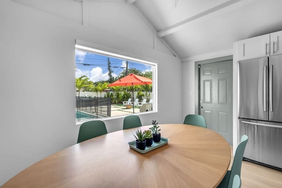 Sunlit dining nook with a round table for four, vaulted ceilings, and a picture window overlooking the pool. A cheerful spot for morning coffee or shared meals.