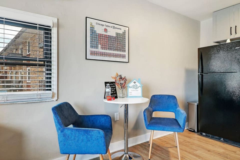This dining area features a small round table and two comfortable blue chairs, perfect for enjoying meals or a cup of coffee. Unique wall art, including a periodic table chart, adds a touch of personality to the space.