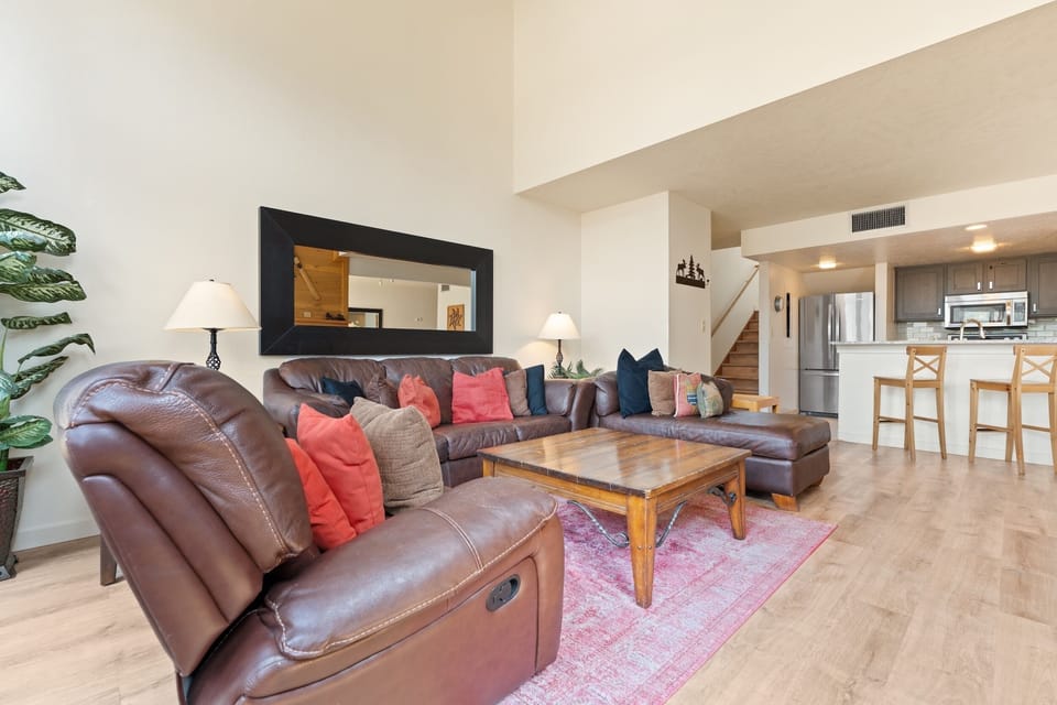 Sink into plush leather sofas with colorful pillows as you unwind in your airy, open-concept living area. The wood coffee table and pink rug add warmth and charm.