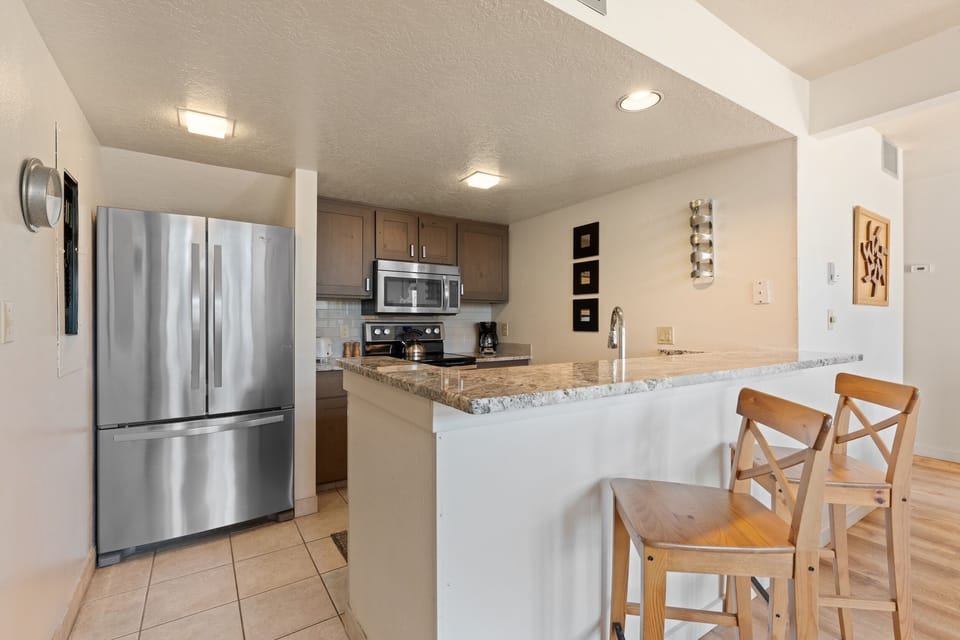 Your fully equipped kitchen awaits with modern stainless steel appliances, granite countertops, and a breakfast bar—perfect for preparing meals and gathering over morning coffee in your home away from home.