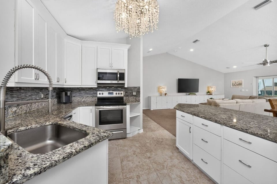 Modern coastal kitchen with granite countertops, stainless steel appliances, spacious island, and open-concept layout overlooking the living room—perfect for preparing meals while spending time with family and friends near Manasota Key Beach.