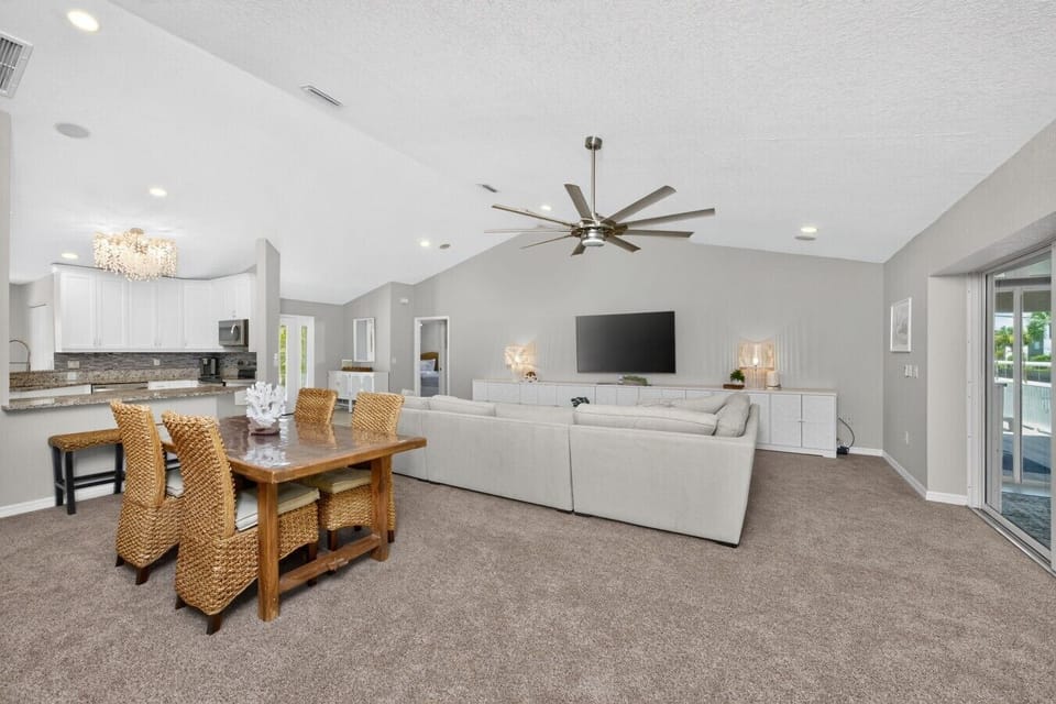 Bright open-concept living, dining, and kitchen area with vaulted ceilings, oversized sectional, Smart TV, breakfast bar, and private balcony access—perfect for entertaining and relaxing after a day at Manasota Key Beach.