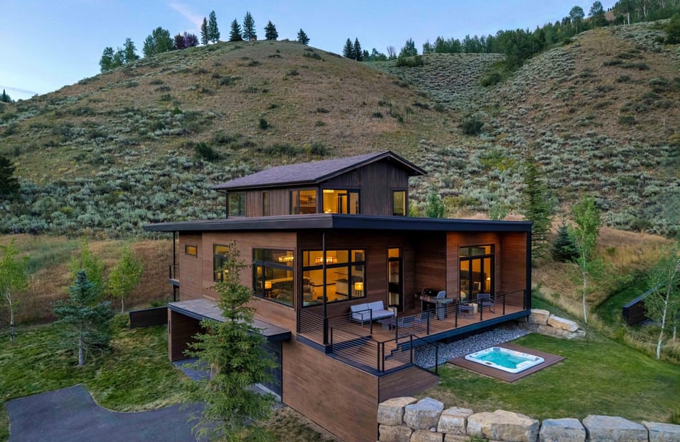 Two-story cabin exterior with a private hot tub, balcony seating, and a stone retaining wall