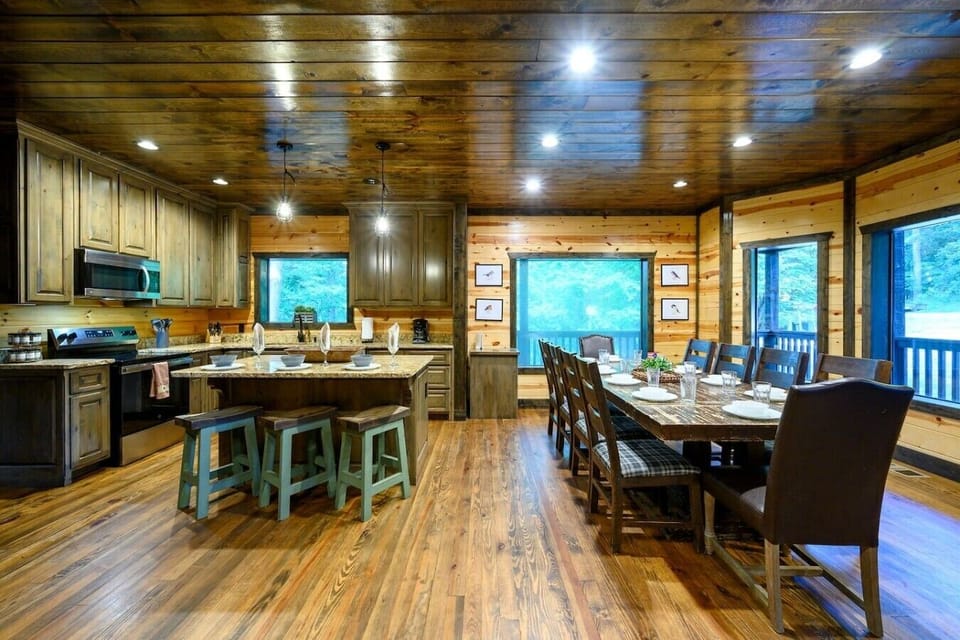 Spacious kitchen with island seating, dining table, and forest-facing windows.