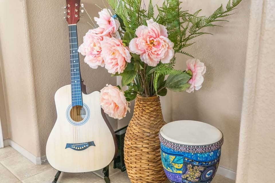 A light-wood acoustic guitar is propped up on a stand on the left. Beside it is a small hand drum