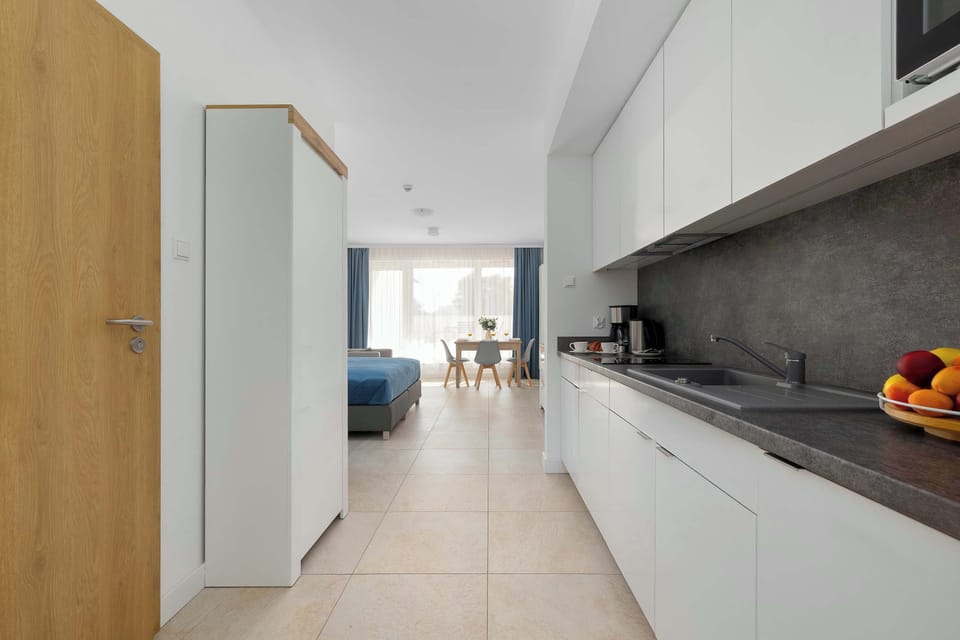 A bright modern kitchen with white cabinets, a dark countertop, and built-in appliances. The open layout creates a welcoming space connected to the rest of the apartment.
