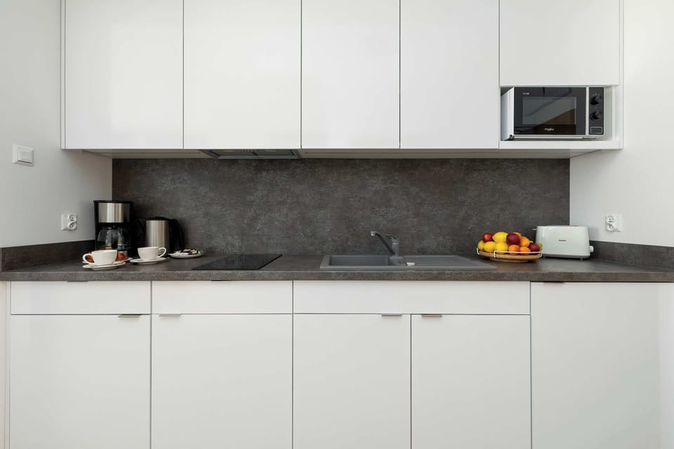 A modern kitchen with sleek white cupboards, a dark backsplash, and practical storage solutions. The space is designed for convenient meal preparation during your stay.