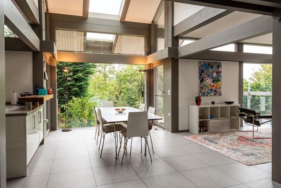 Sunlit dining hall under soaring beams with garden views