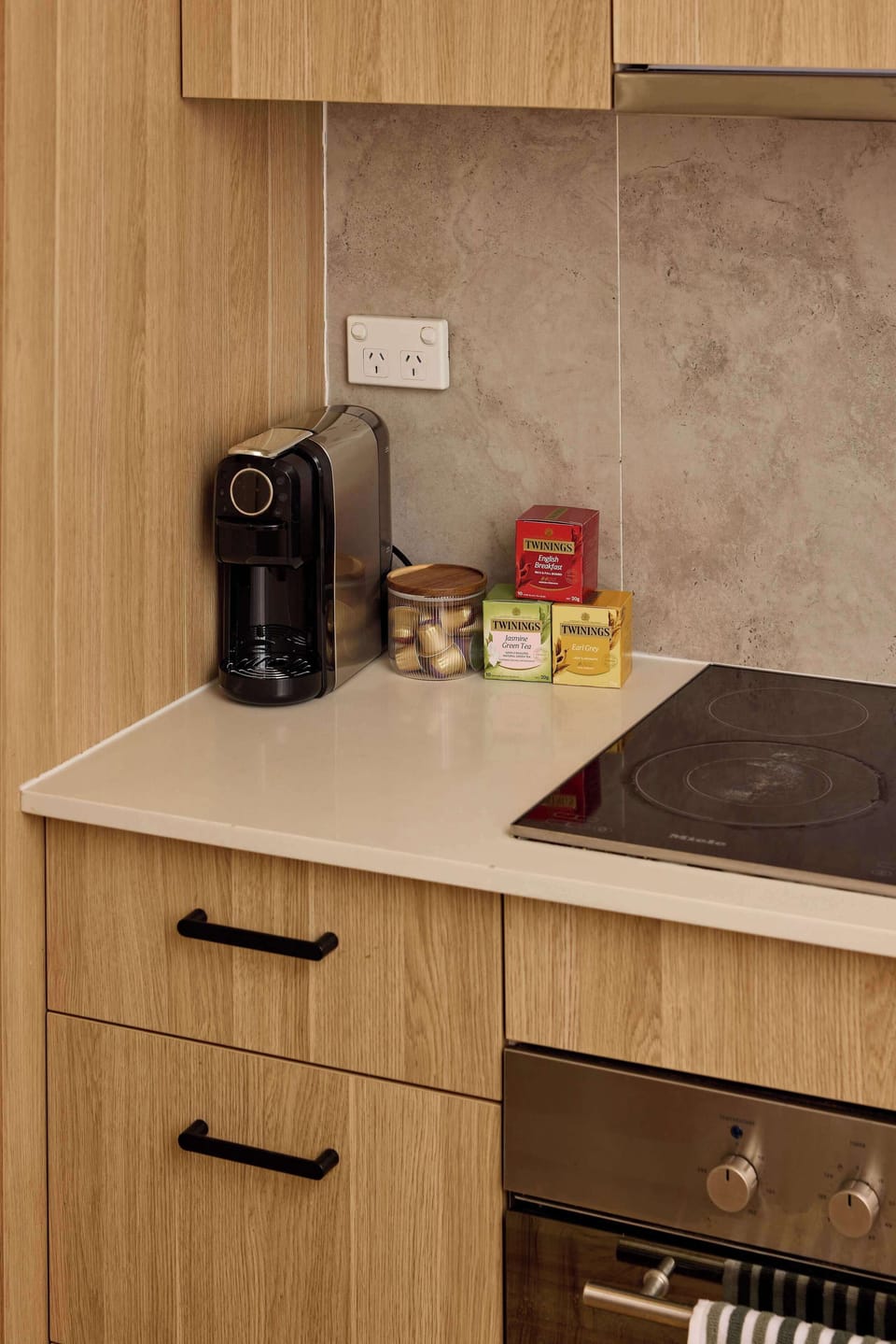Start your morning right with complimentary coffee and tea supplies set alongside an espresso machine in this modern kitchen corner featuring light wood cabinetry.