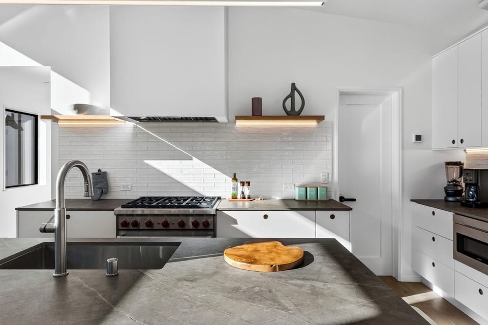 Close-up of the cooking area featuring a high-end stainless steel gas range, subway tile backsplash, and floating wooden accent shelves.