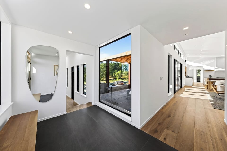 Bright entryway with dark tile flooring, a geometric wall mirror, and a floor-to-ceiling picture window framing the outdoors.