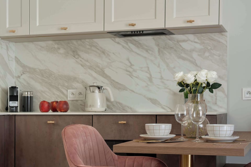 A dining area with a modern kitchen and elegant marble backsplash. The space is bright and tastefully decorated.