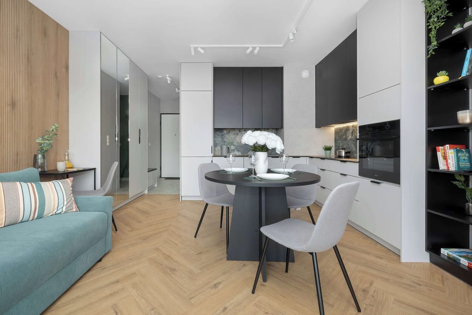 Looking toward the entrance, the open floor plan reveals a compact desk nook, the kitchen, and a dining set. Wooden wall paneling adds warmth to the interior.