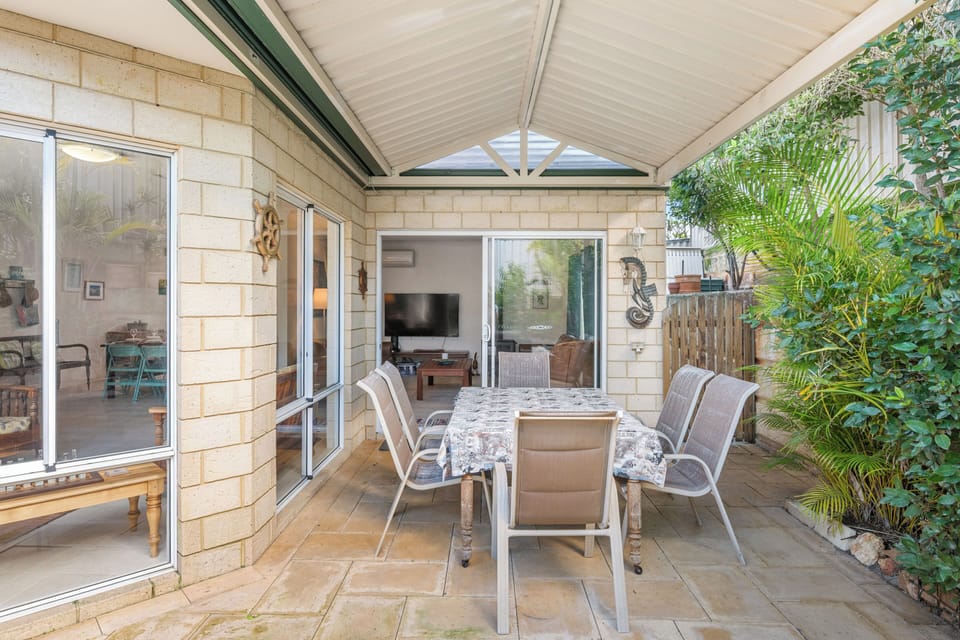 Enjoy alfresco dining and relaxation on this covered patio, complete with an outdoor dining set and surrounded by lush greenery.