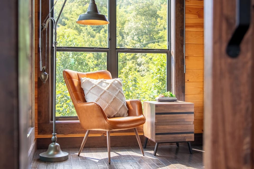 Curl up in your cozy reading nook with sunlight streaming through large windows, where lush green views and warm leather invite you to unwind completely.