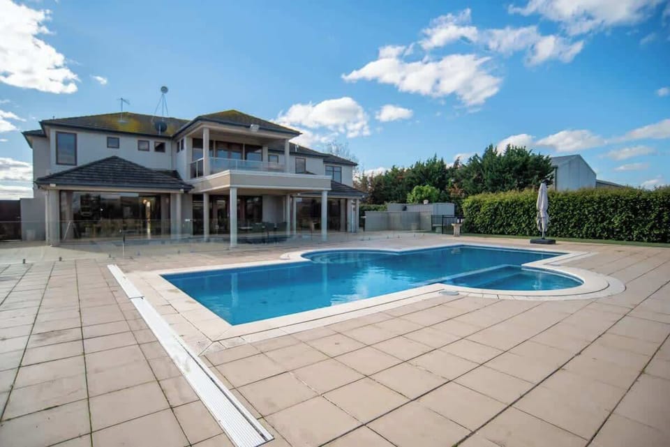 Resort-style pool with fully fenced pool area, spacious paved surrounds, and the full two-storey manor as backdrop.