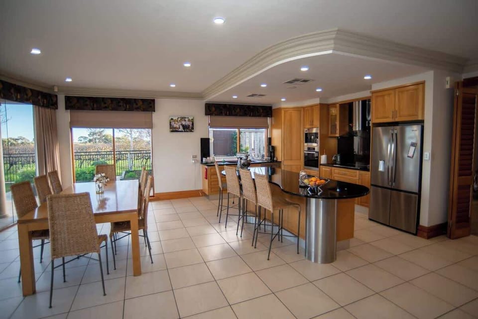 Fully equipped gourmet kitchen with stainless steel appliances, black granite island bench with bar seating, and dining table for eight with vineyard views. Ground floor.