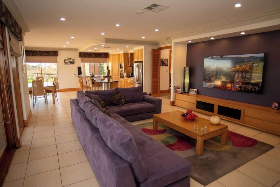 Open-plan living and dining area with large sectional sofa, big-screen TV, and gourmet kitchen with black granite island bench. Ground floor.